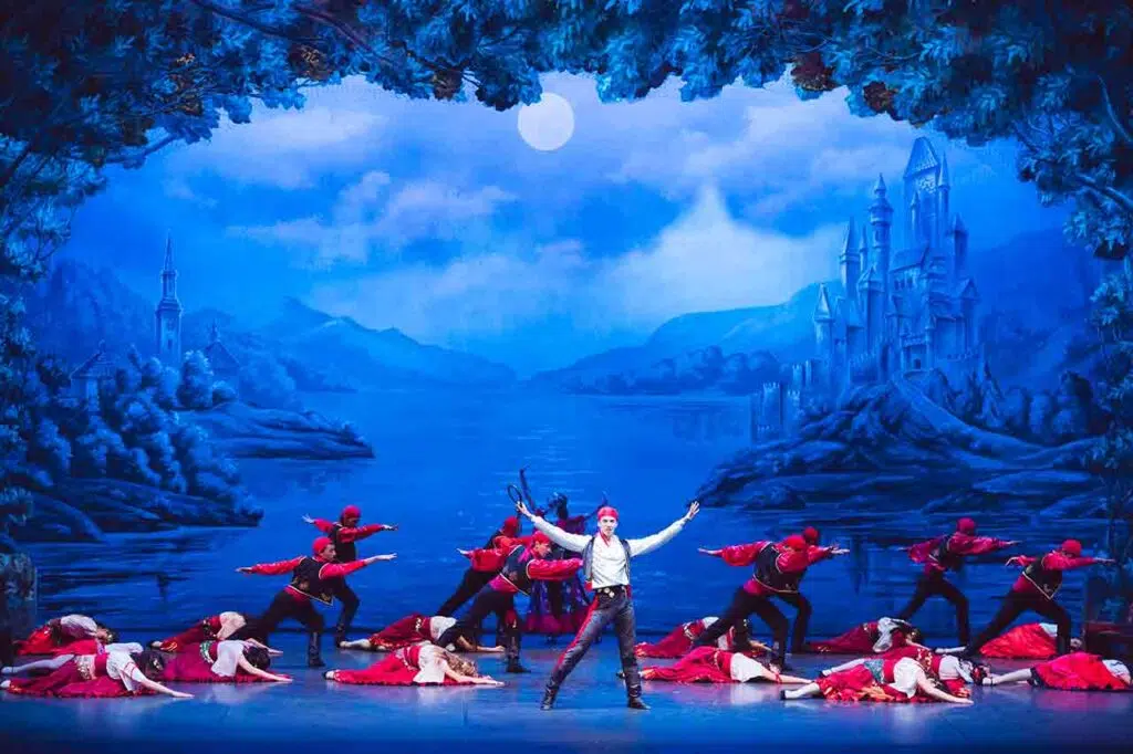 Danzatore al centro del palcoscenico circondato dal corpo di ballo in costumi rossi