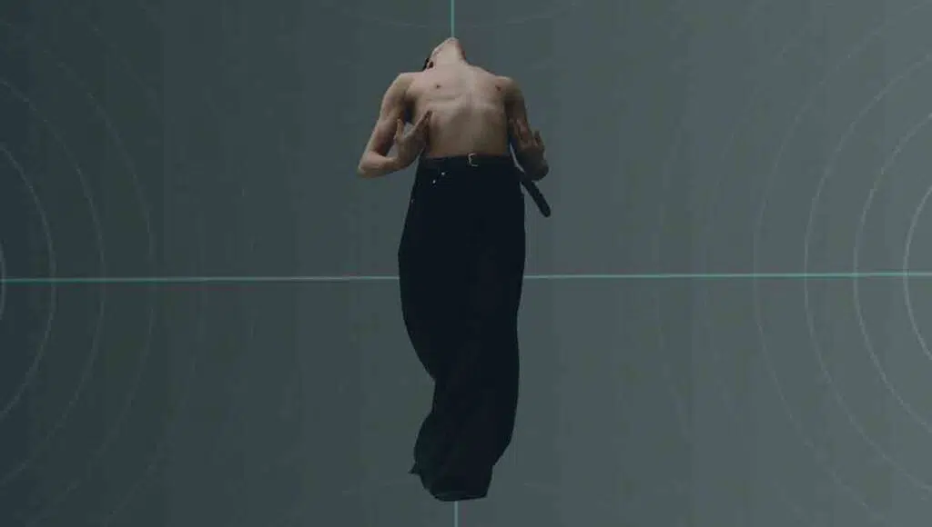 Performer a torso nudo si inarca davanti a una proiezione di linee luminose durante To Be Feedback